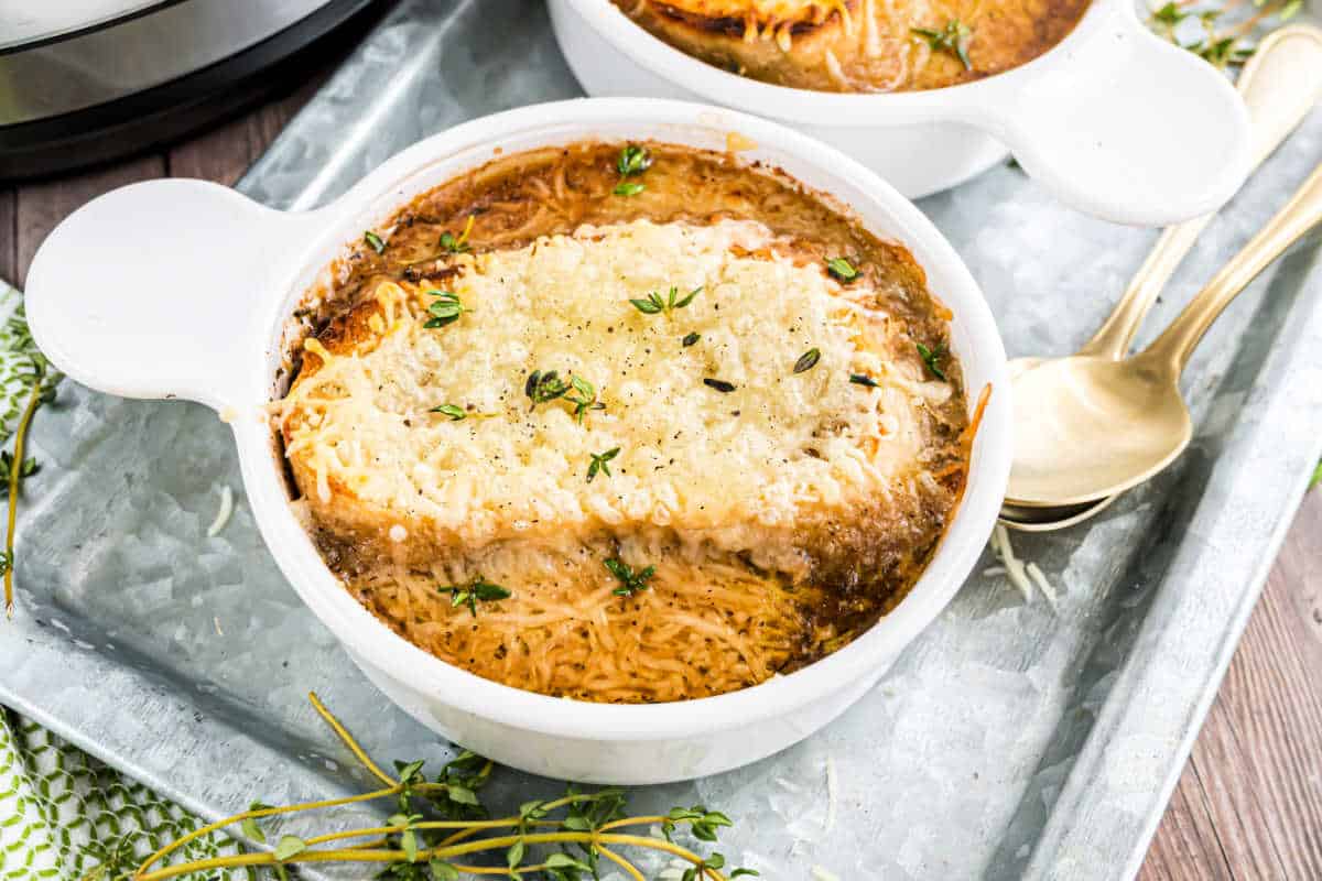 A bowl of classic french onion soup topped with melted cheese and fresh herbs, with a spoonful taken out for a perfect comfort meal.