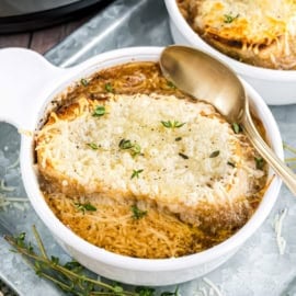 A steaming bowl of french onion soup topped with melted cheese, toasted bread, and fresh herbs sits invitingly, with a spoon beside it.