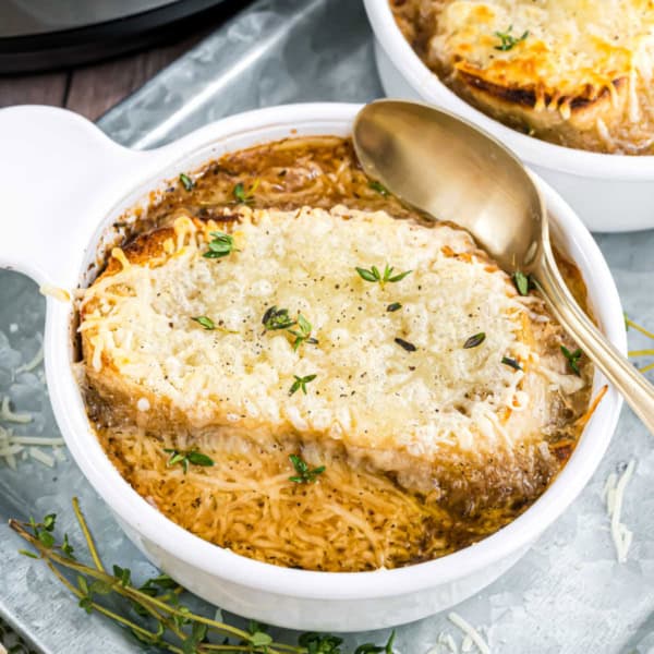 A steaming bowl of french onion soup topped with melted cheese, toasted bread, and fresh herbs sits invitingly, with a spoon beside it.