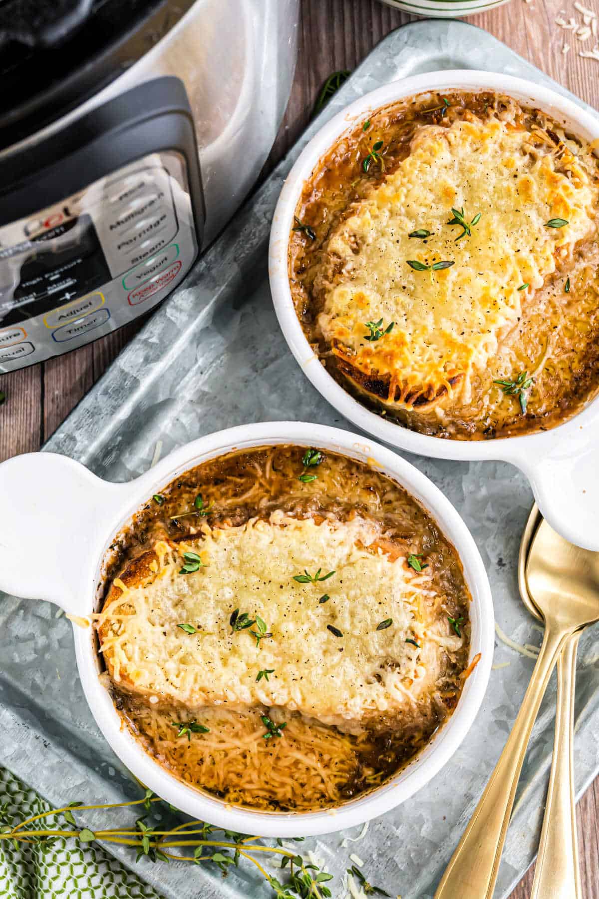 Two bowls of french onion soup with melted cheese on top, served alongside an Instant Pot and gold spoons.