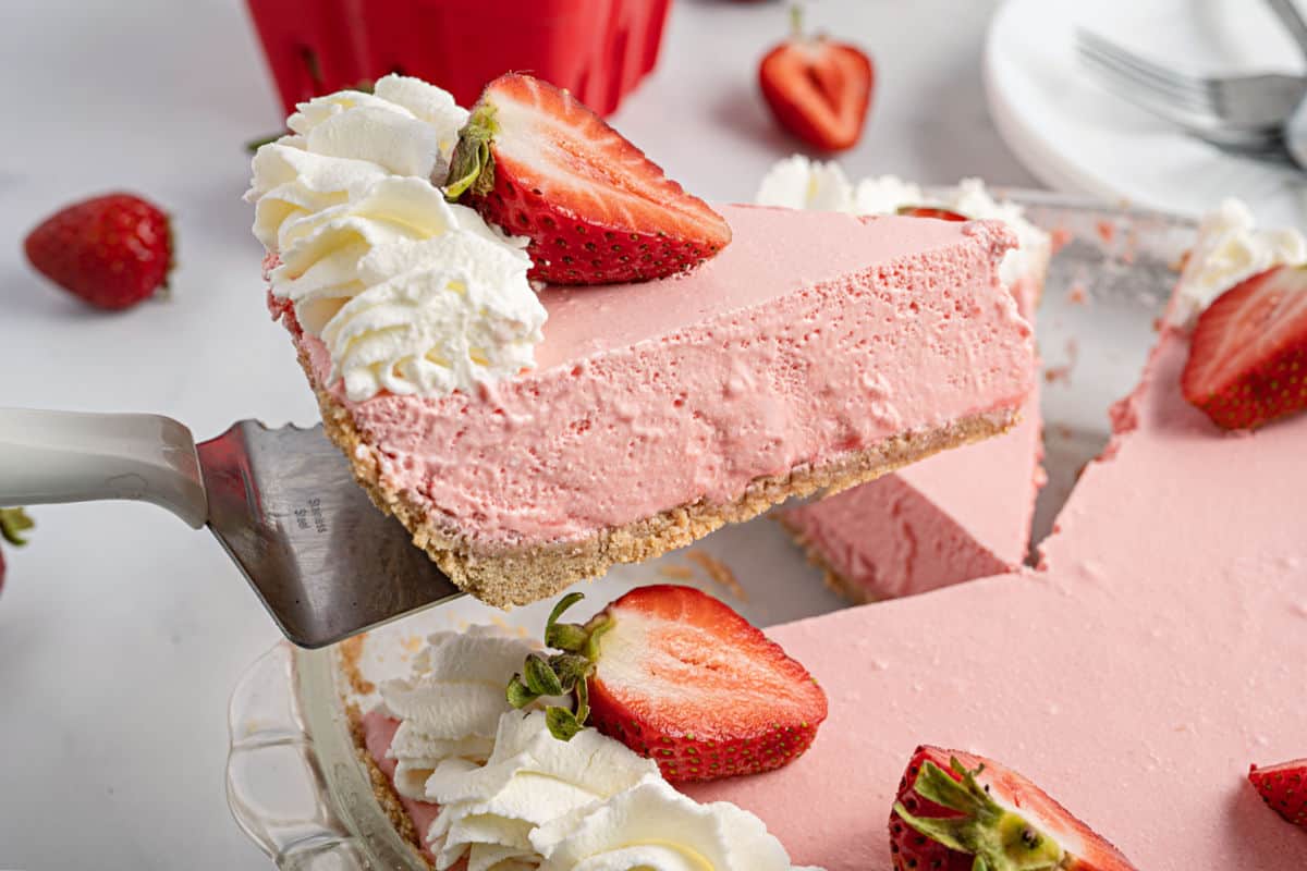 Slice of jello pie with strawberries being lifted out of pie plate.