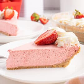 Slice of strawberry jello pie with fresh whipped cream and strawberries on a white plate.