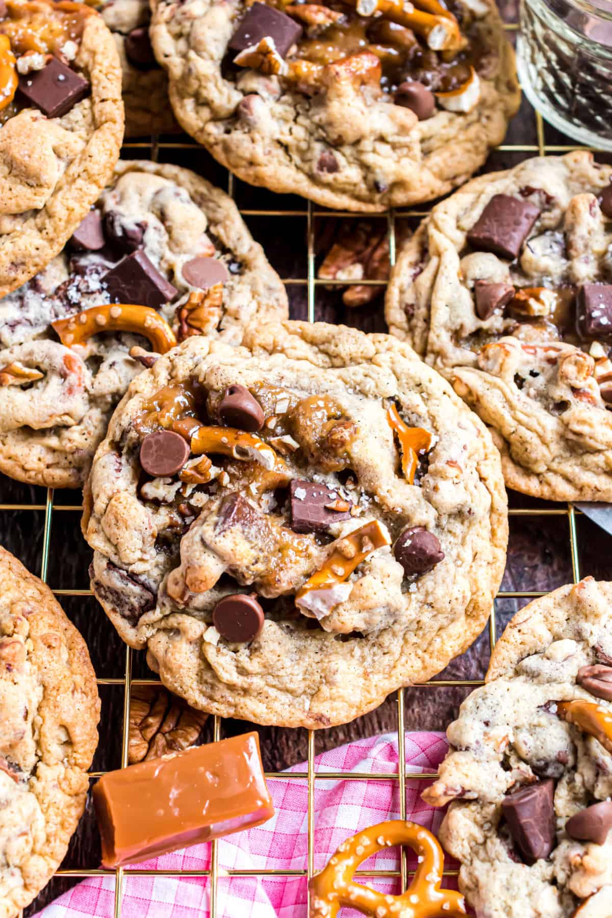 Chocolate chip cookies stuffed with caramel, pecans, chocolate, and pretzels on a wire cooling rack.