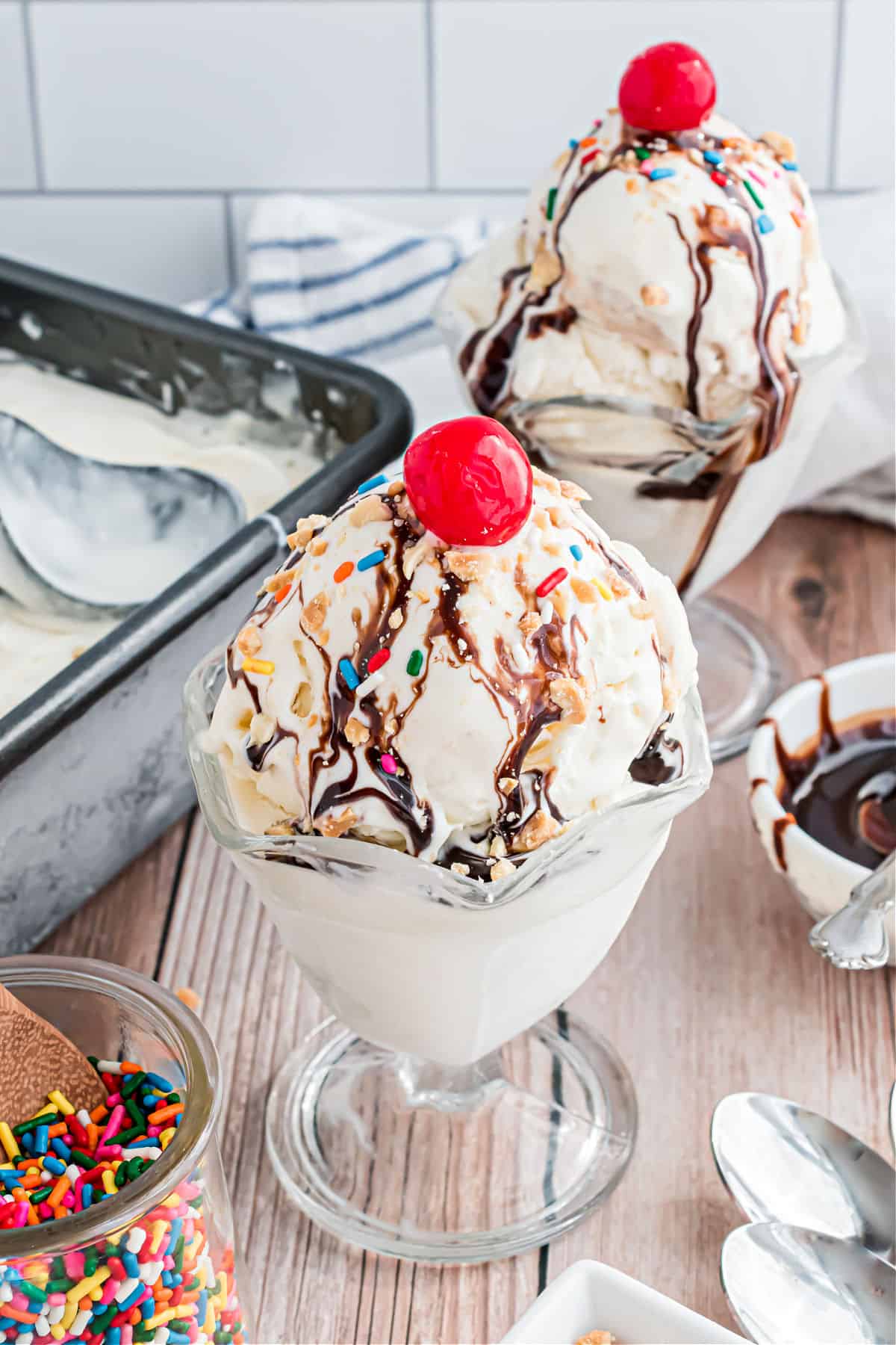 Dishes of vanilla ice cream with chocolate syrup, nuts, and cherry on top.