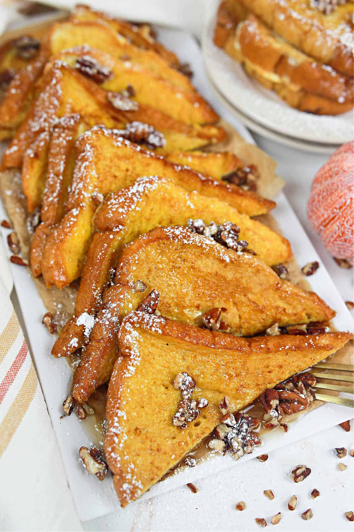Pumpkin French Toast cut into triangles and topped with pecans, powdered sugar, and syrup.