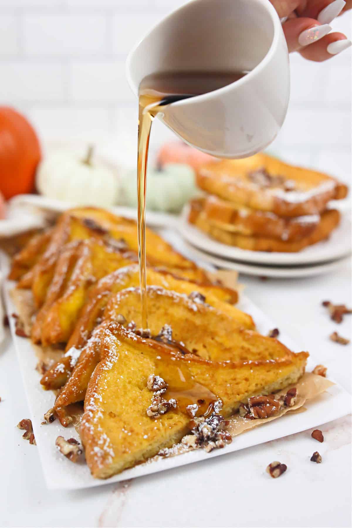 Pumpkin french toast on a white platter being drizzled with maple syrup.
