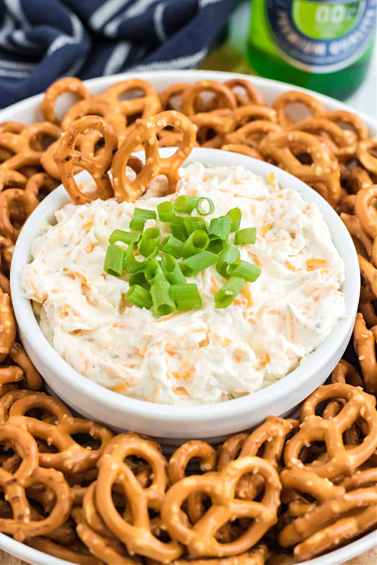 Cheese dip in a white bowl surrounded by pretzel twists for dipping.