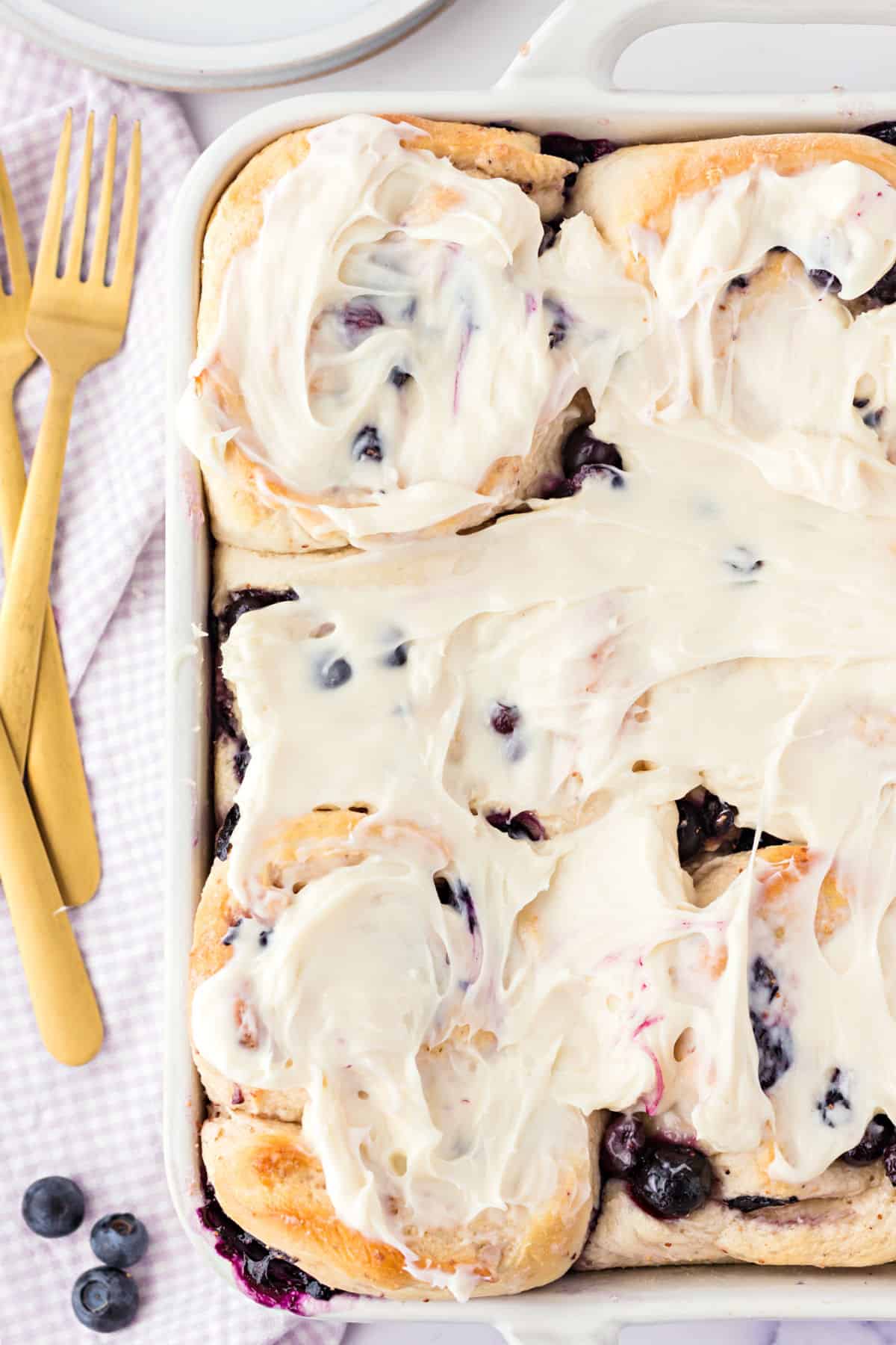 Blueberry cinnamon rolls topped with cream cheese icing in a white baking dish.