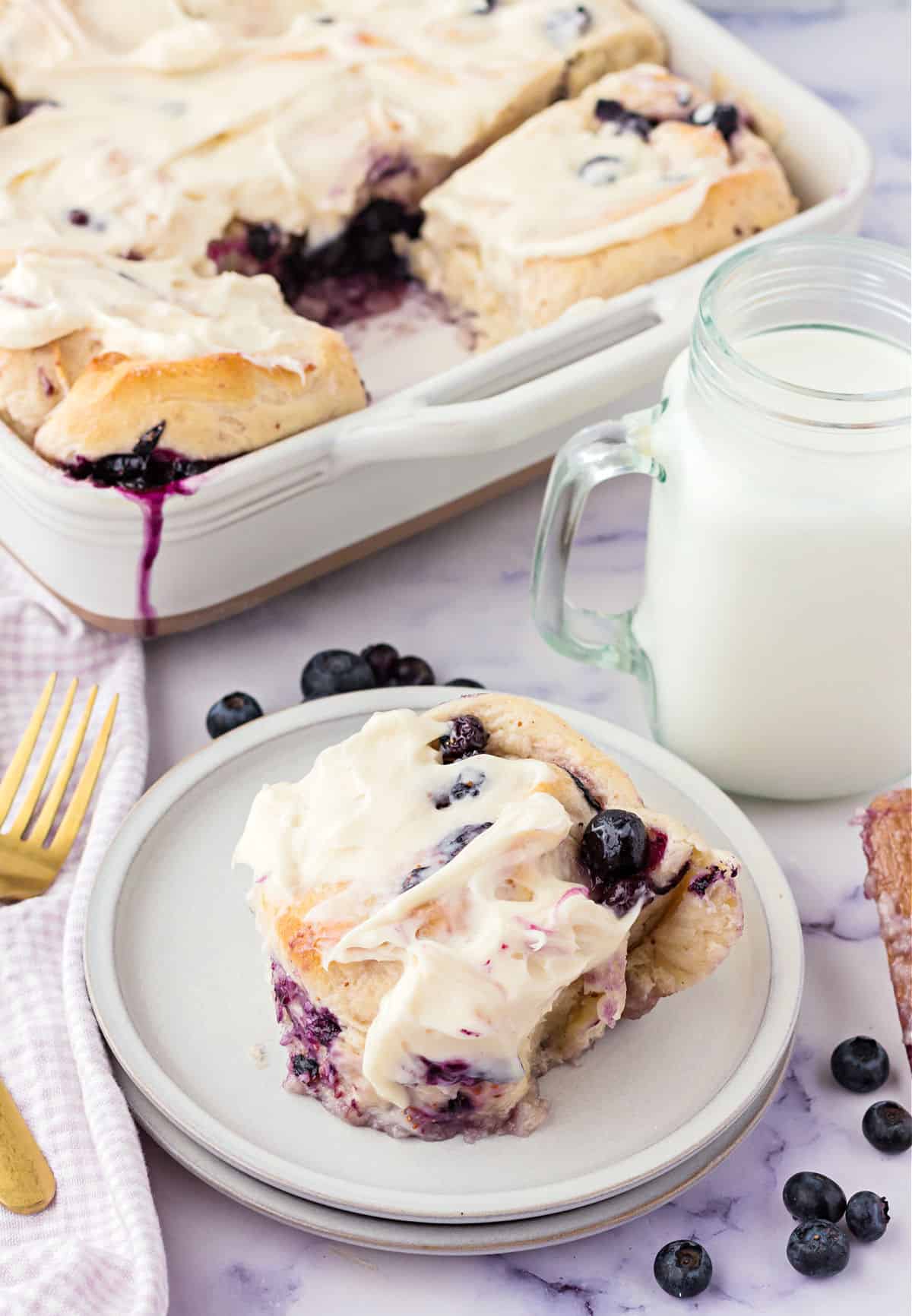 Gooey blueberry roll topped with icing served on a white plate.