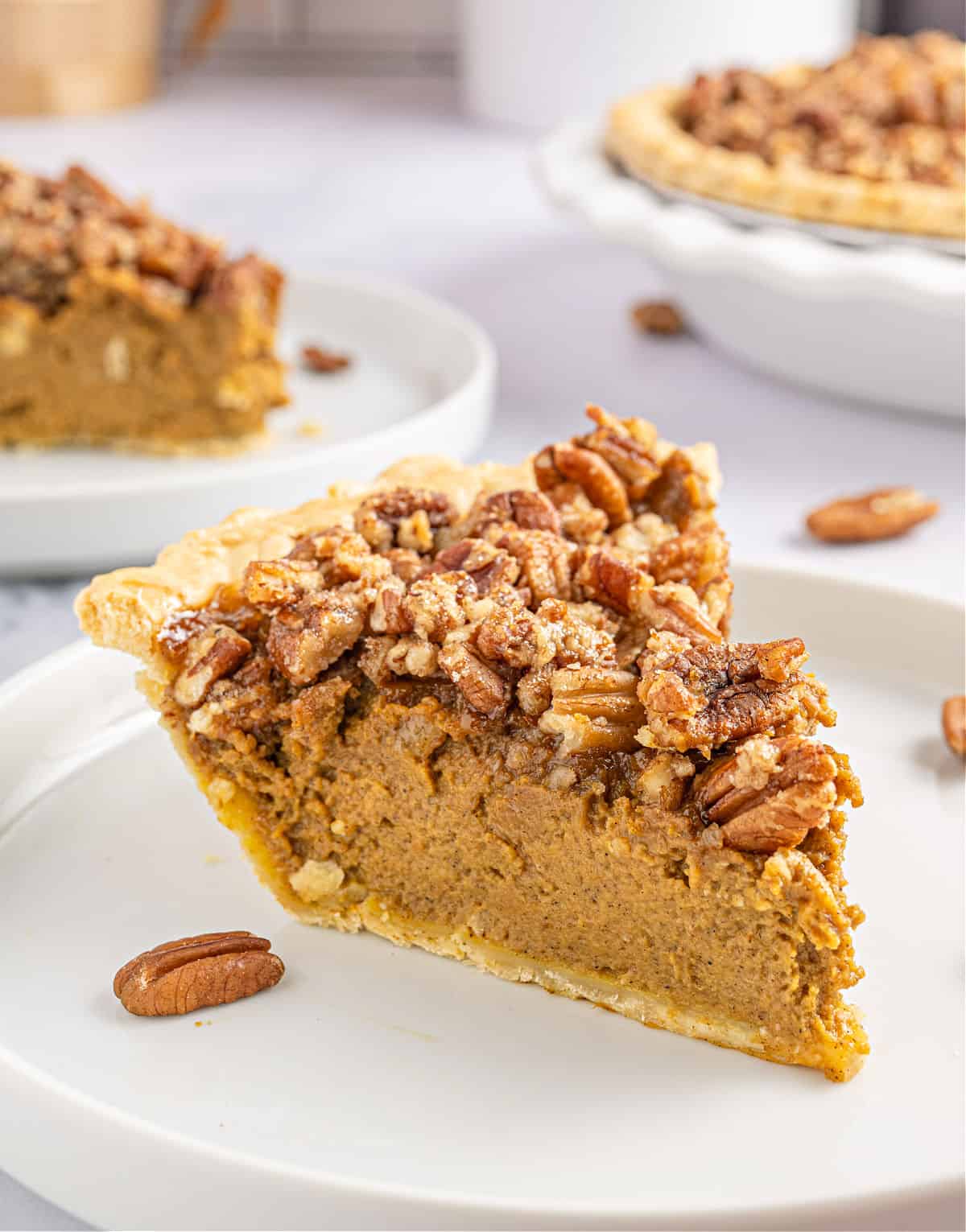 Pumpkin pie with pecan topping cut into a slice and served on a white plate.
