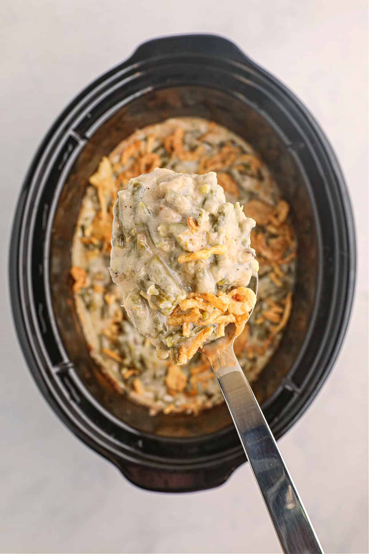 Black crockpot with a spoonful of green bean casserole being scooped out.