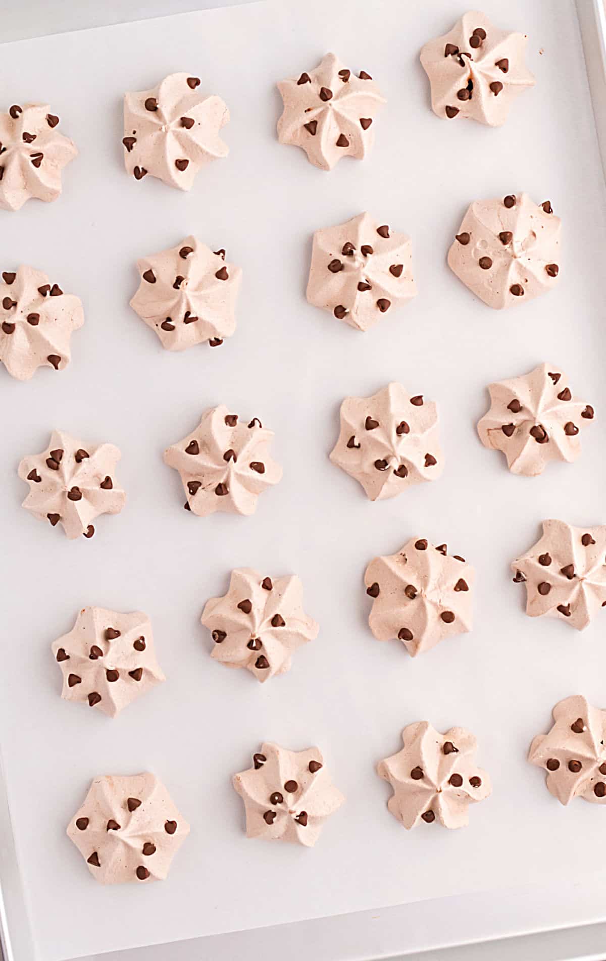 Chocolate meringue cookies with chocolate chips on parchment paper lined cookie sheet.