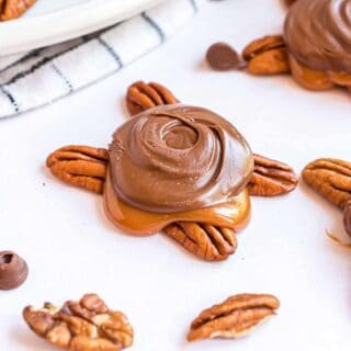 Pecans topped with caramel and chocolate on parchment paper.
