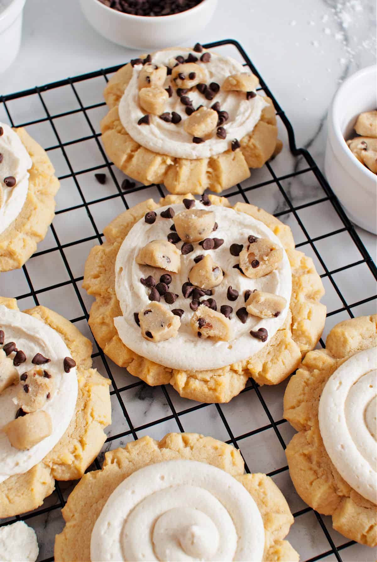 Sugar cookies topped with cookie dough and frosting on a wire rack.