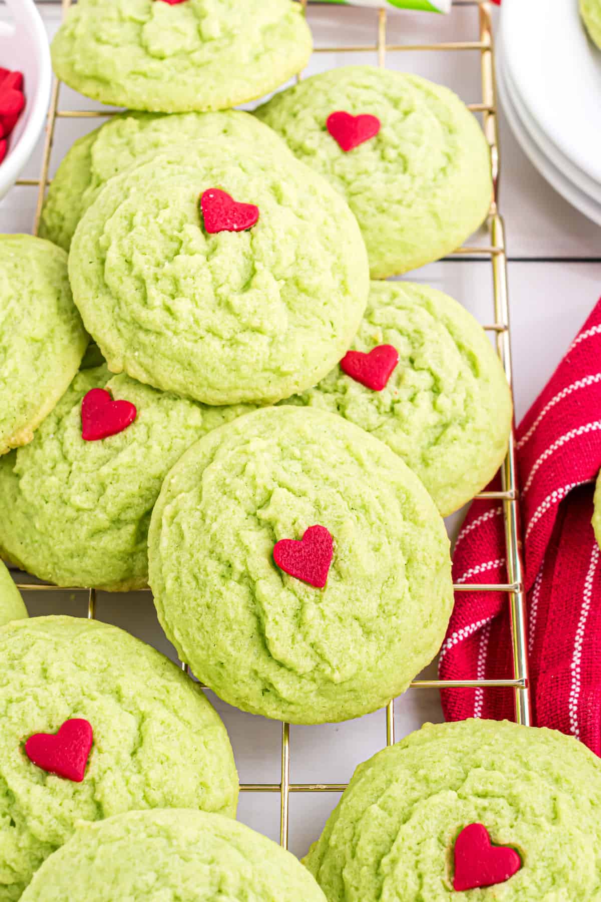 Green cookies with a red heart stacked on a wire cooling rack.