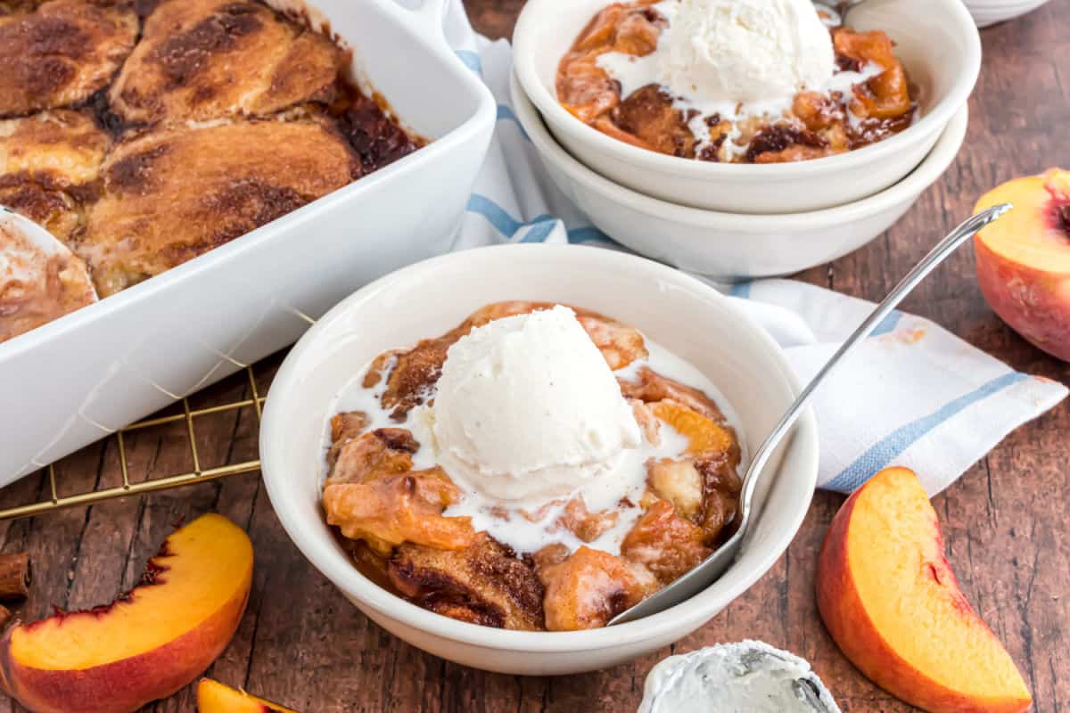 Peach cobbler in white bowls with vanilla ice cream on top.