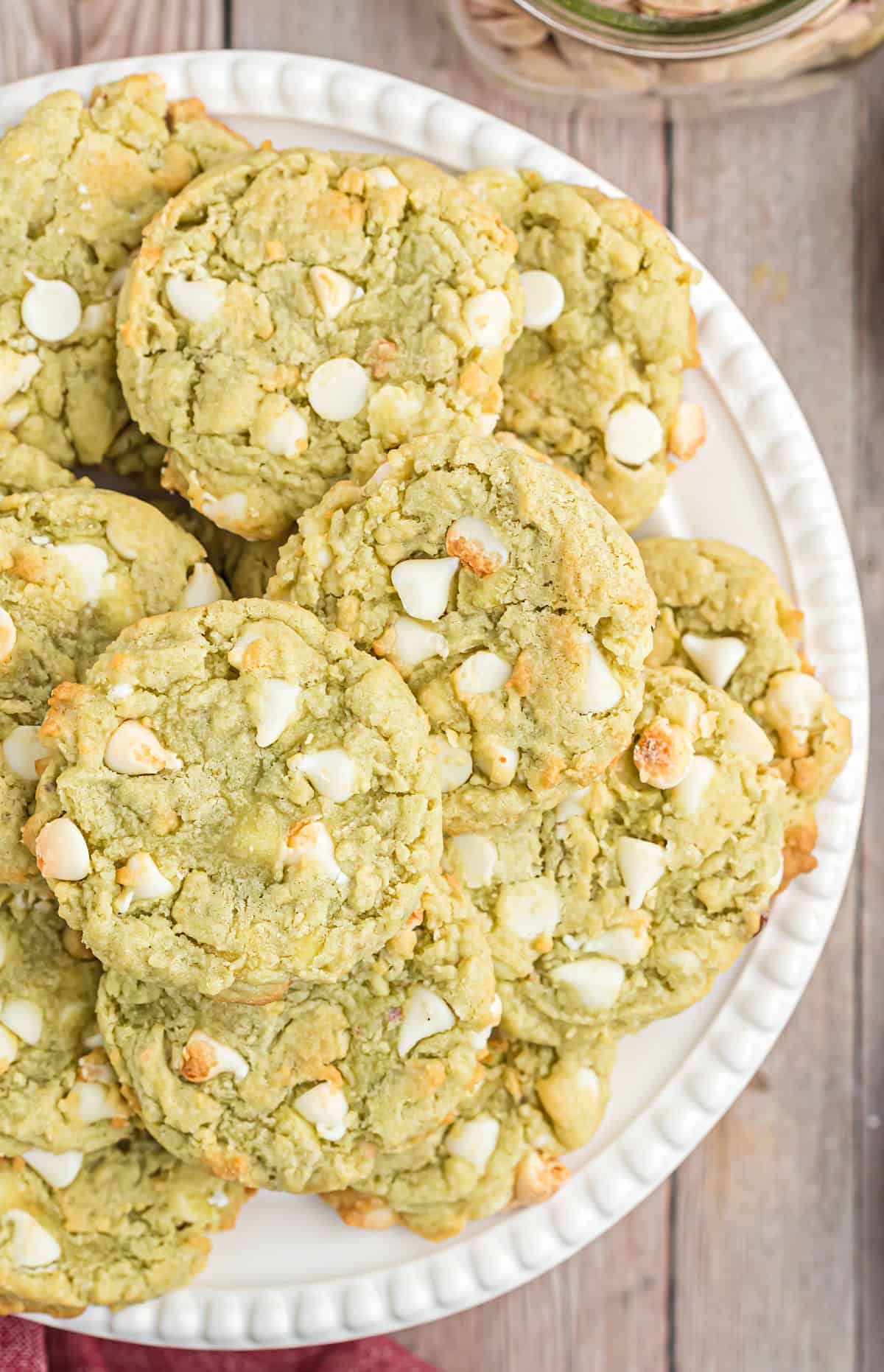 Pistachio cookies with white chocolate chips stacked on a white serving platter.