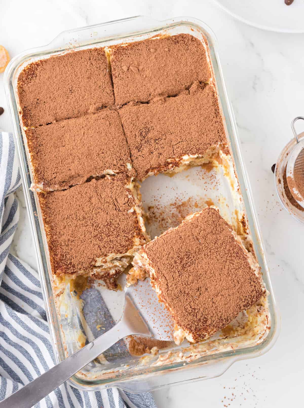 13x9 glass baking dish with large slices of tiramisu and a spatula.