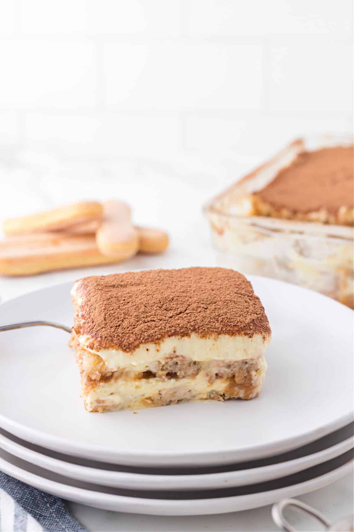 Slice of tiramisu on stack of white plates.