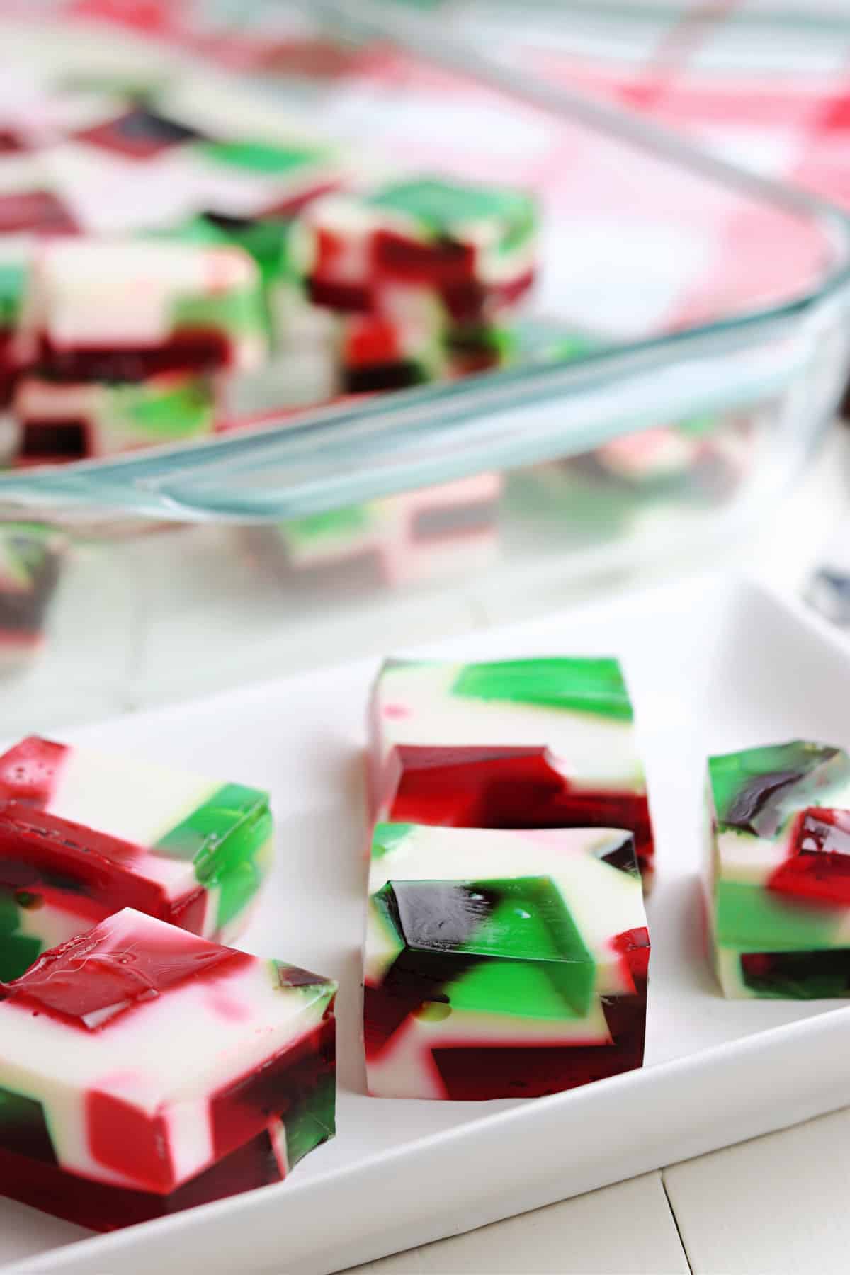 Squares of broken glass jello bites on a white platter.