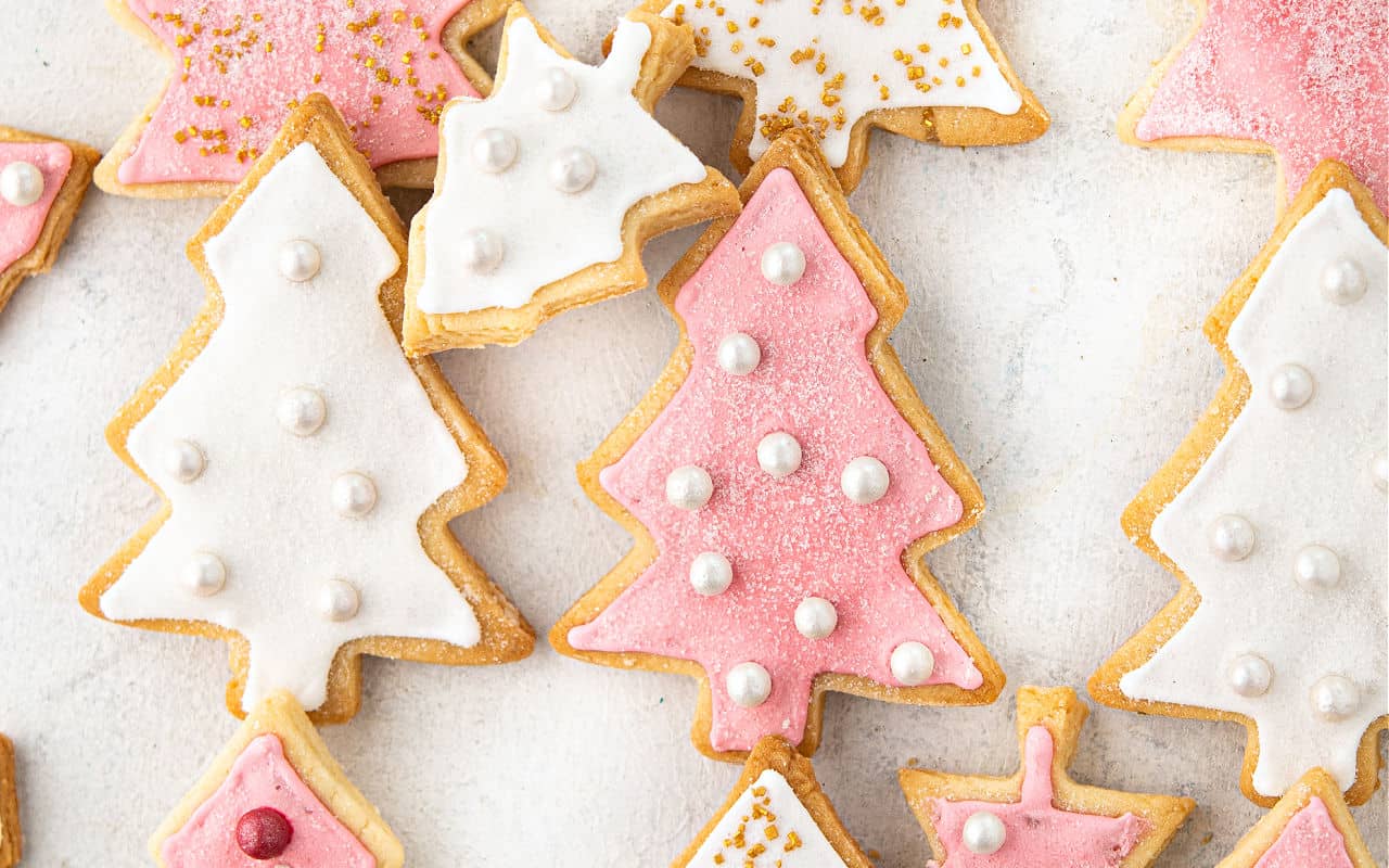 Christmas tree shaped cookies with pink and white icing on parchment paper.