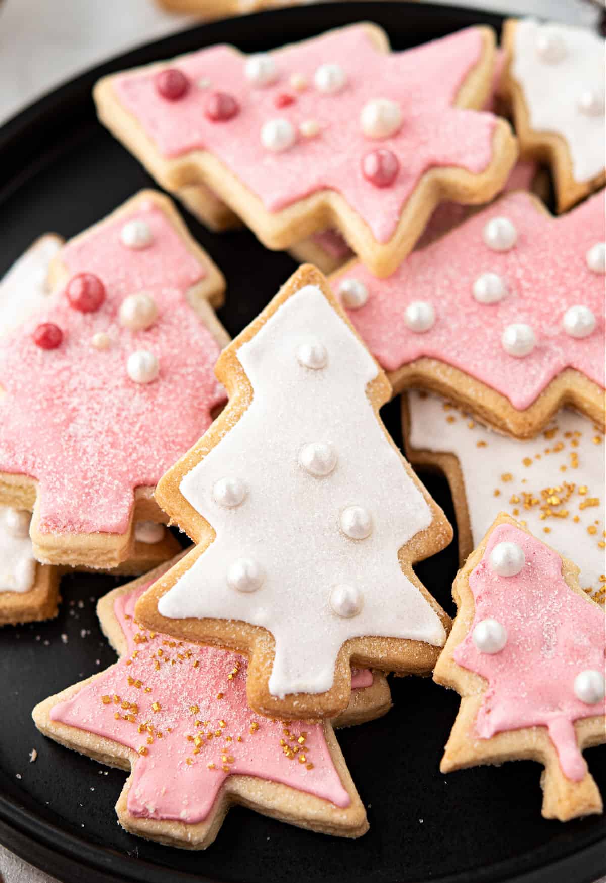 Pink and white Christmas tree shaped sugar cookies on a black plate.