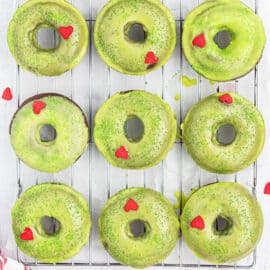 Grinch Donuts are baked chocolate donuts, dusted with green sugar and finished with a red candy heart. These easy holiday donuts are delicious enough to make anyone's heart grow three sizes!