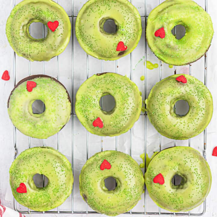 Le Grinch Donuts sono ciambelle al cioccolato cotte, spolverate di zucchero verde e rifinite con un cuore di caramella rossa.  Queste facili ciambelle natalizie sono abbastanza deliziose da far crescere il cuore di chiunque!