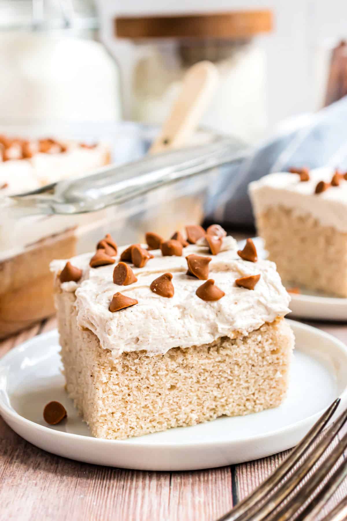 Slice of cinnamon cake with frosting and cinnamon chips served on a white plate.