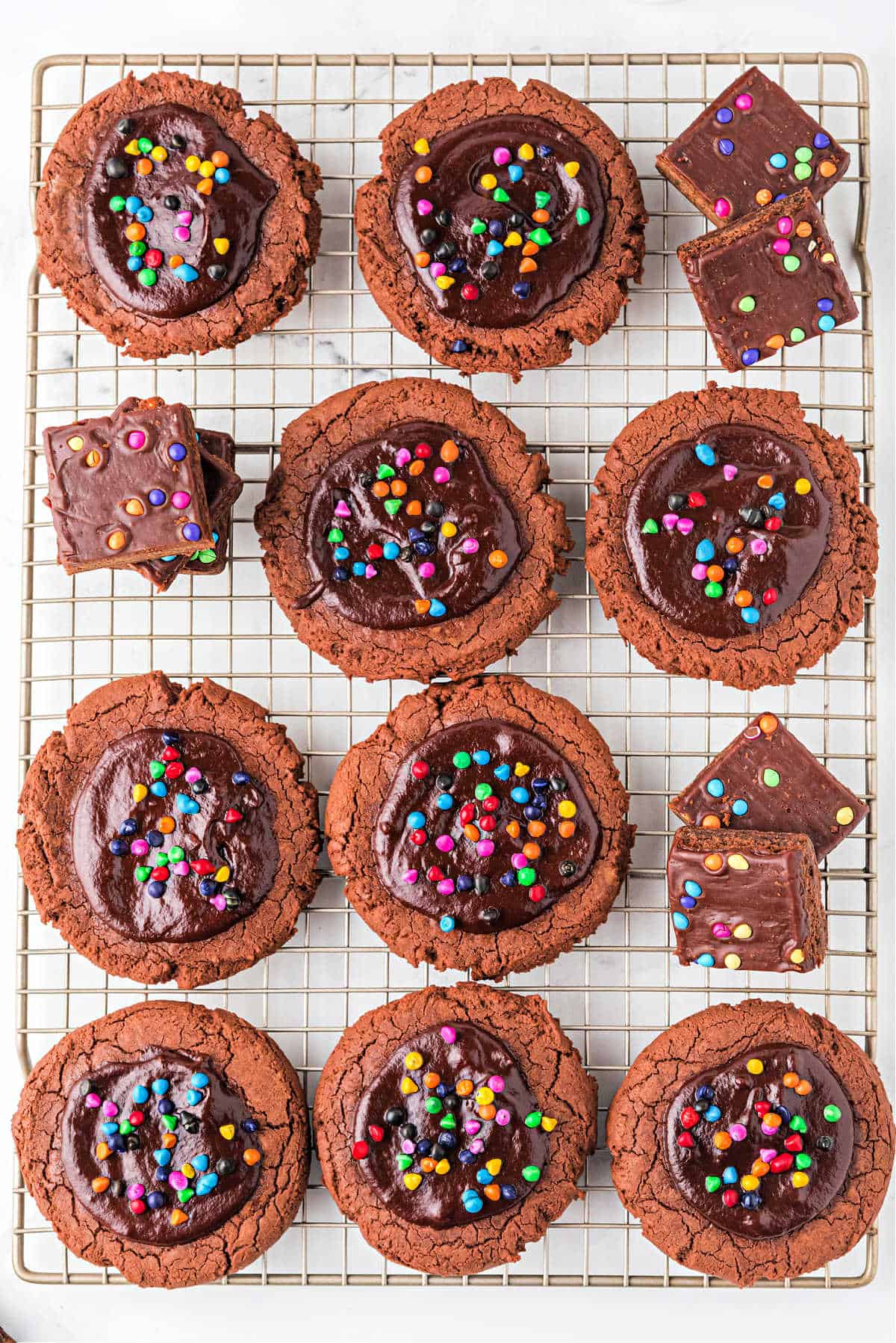 Chocolate cookies with ganache and rainbow chips on a wire cooling rack.