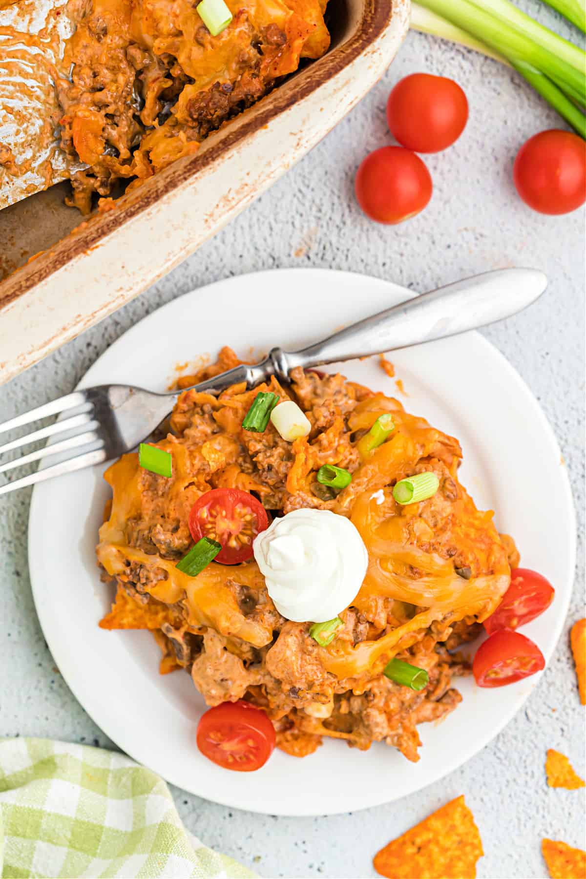 Scoop of Doritos casserole on a white plate with sour cream and cherry tomatoes.