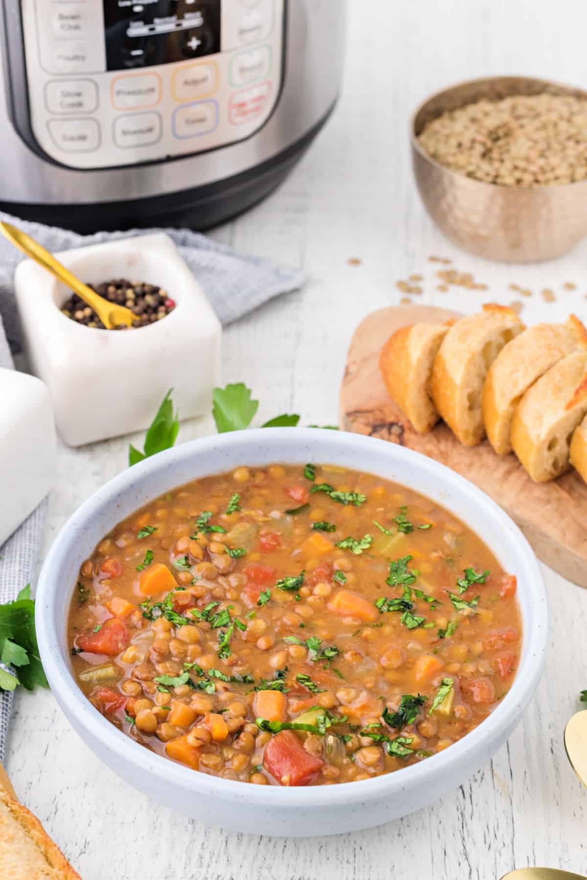 Lentil soup in a white bowl with crusty french bread on the side.