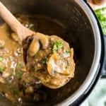 A wooden spoon lifts creamy mushroom gravy from a pot of instant pot salisbury steak, garnished with fresh parsley.