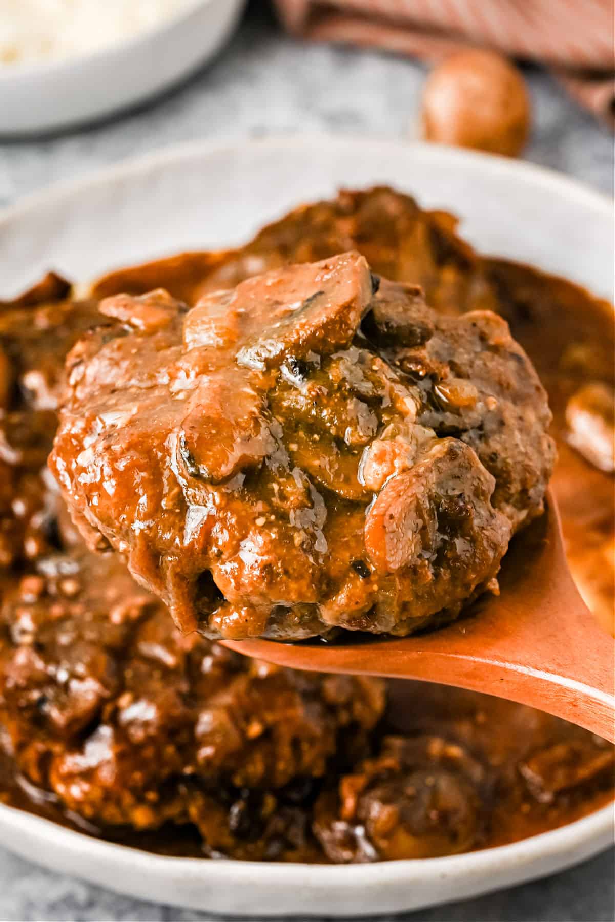 Salisbury steak with mushroom gravy in white bowl with wooden spoon to serve.