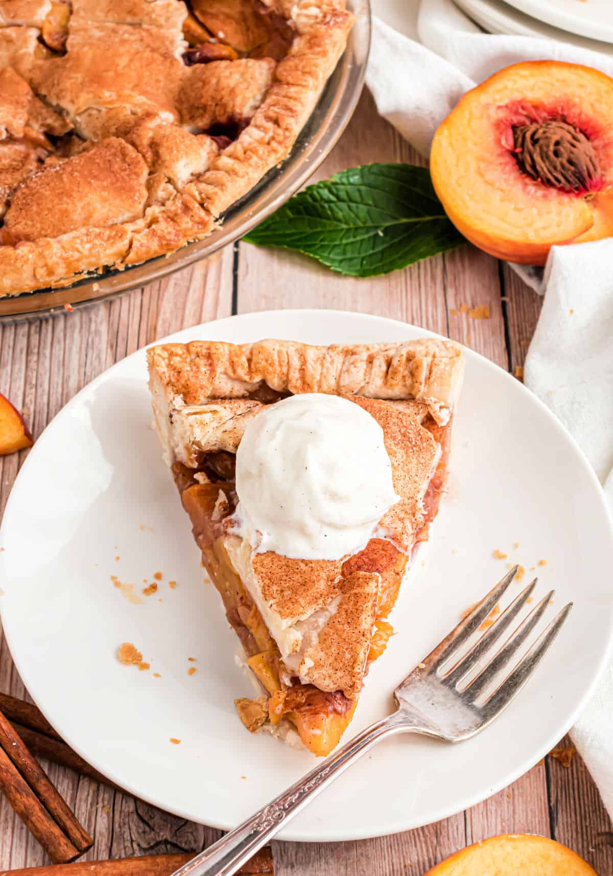 Slice of peach pie with a scoop of vanilla ice cream on top.