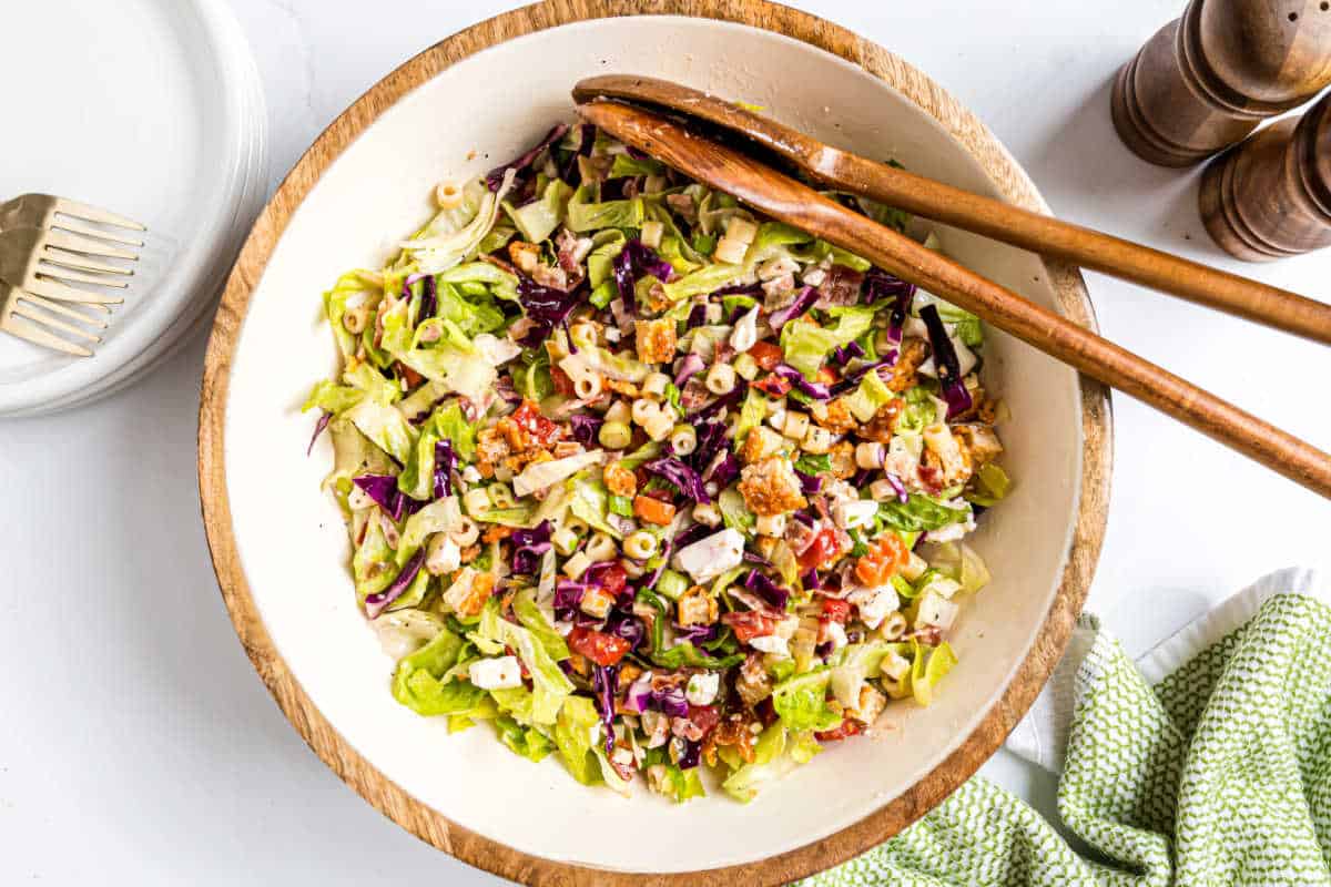A large bowl of chopped salad with pasta, vegetables, and wooden salad tongs on top—perfect for pairing with a hearty instant pot salisbury steak.