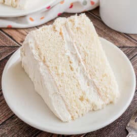Slice of white layer cake with vanilla frosting on a white plate.