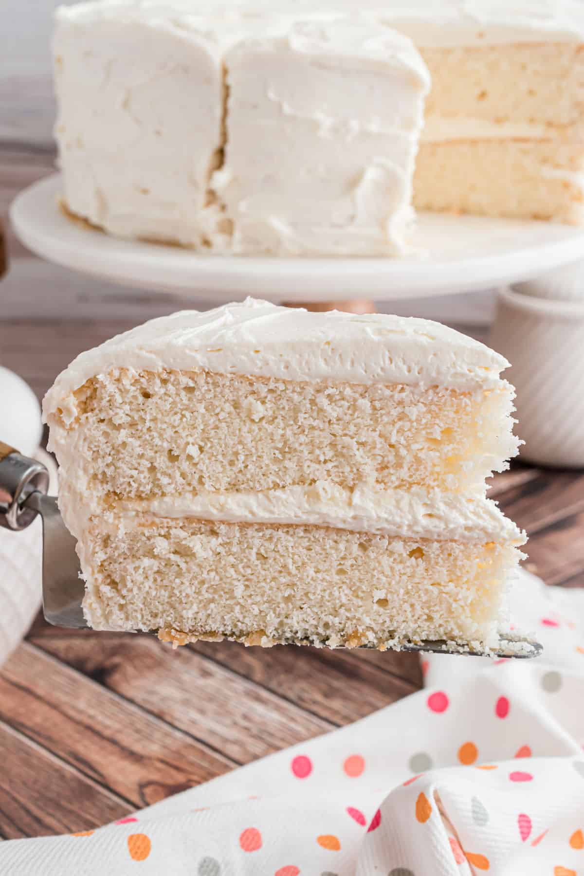 Slice of white cake with vanilla frosting on a spatula to serve.