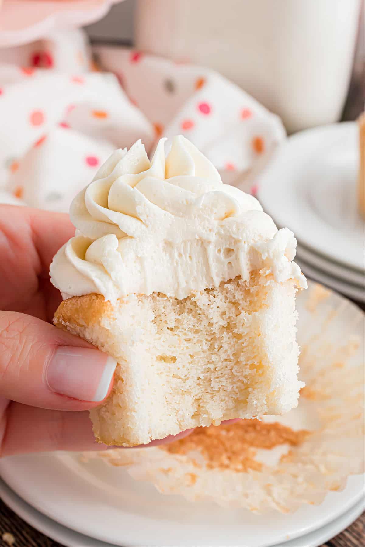 A bite taken out of a white cupcake with vanilla frosting.