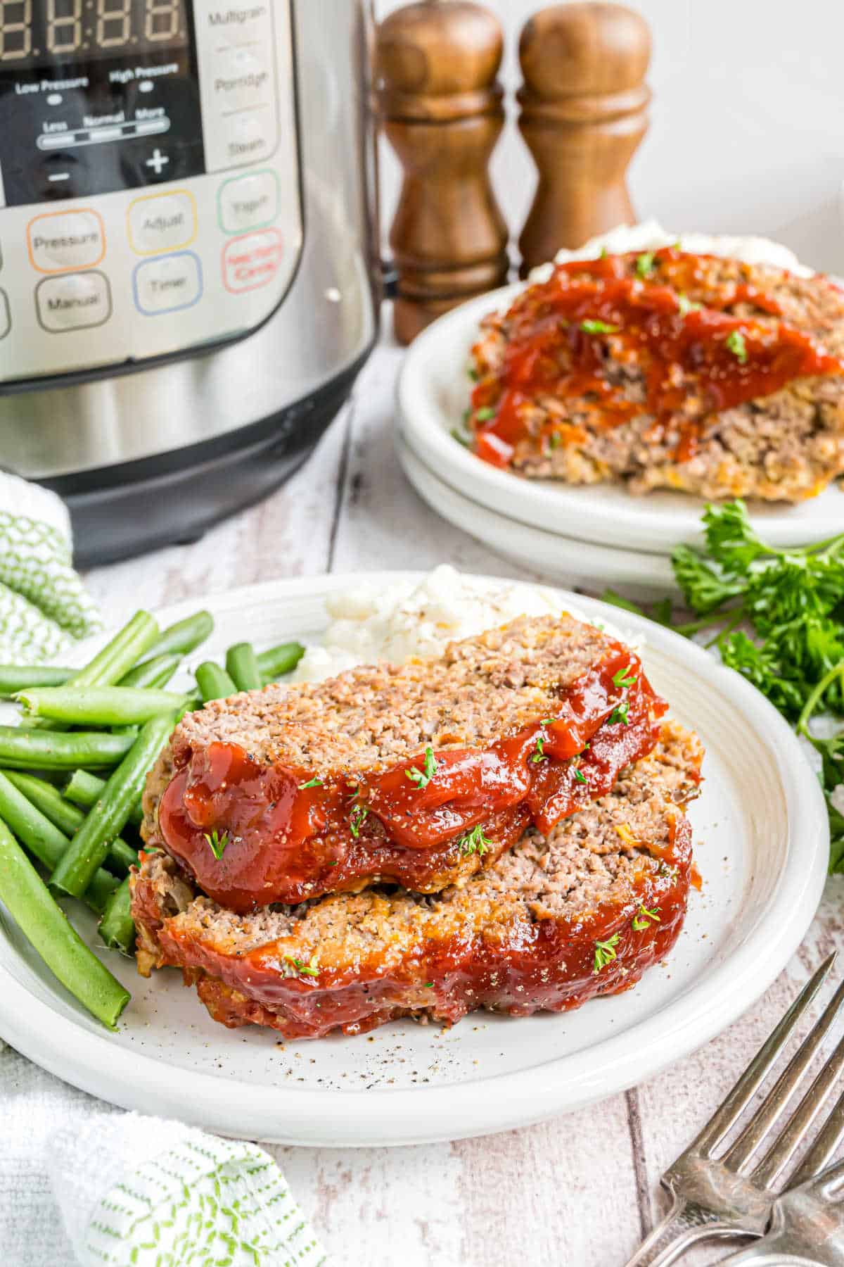Two slices of meatloaf on a white plate with green beans.