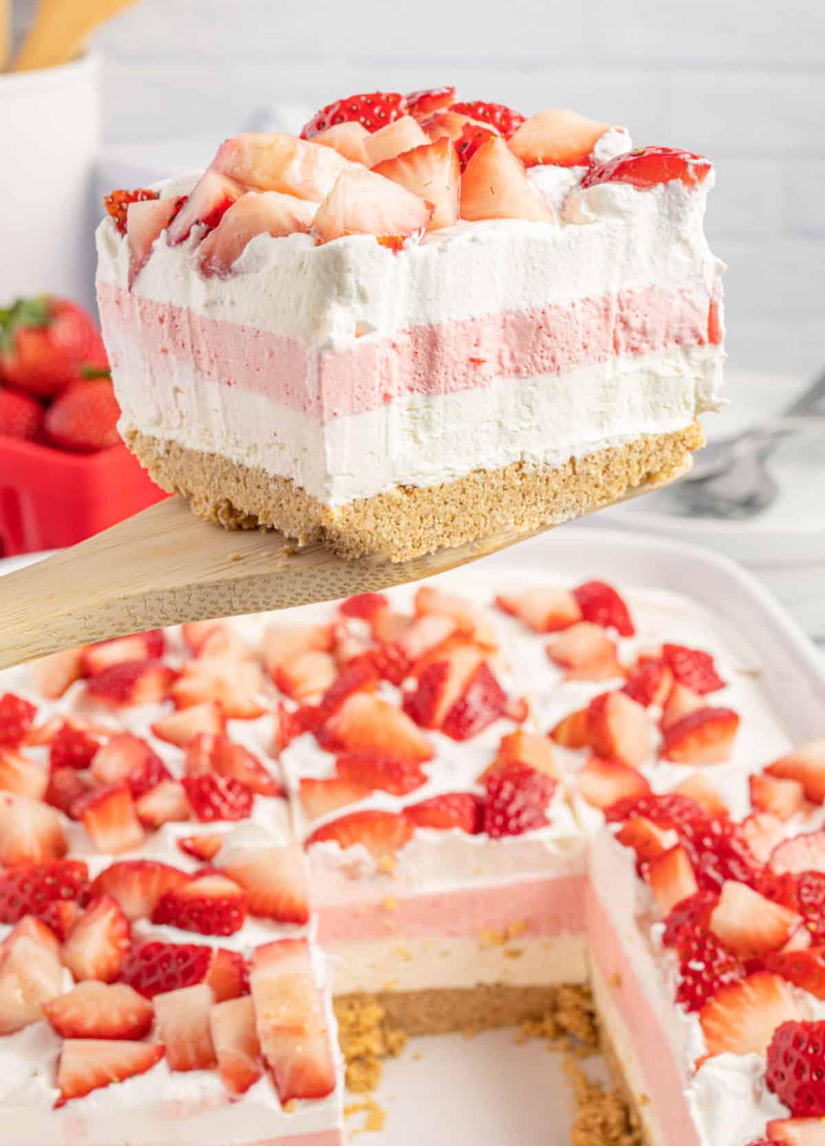 Slice of strawberry desserts being lifted out of white dish.