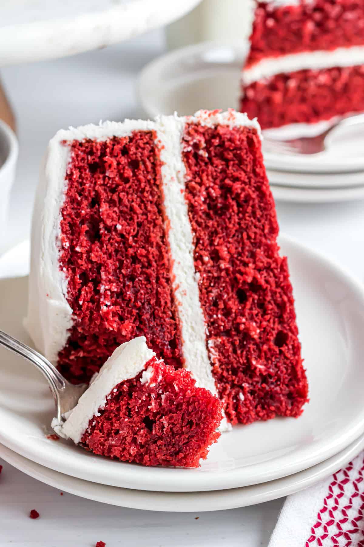Slice of red velvet cake on a white plate with a bite taken.