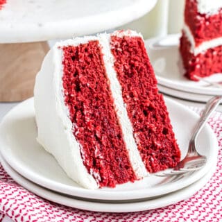 Two layer red velvet cake with cream cheese frosting on a plate.