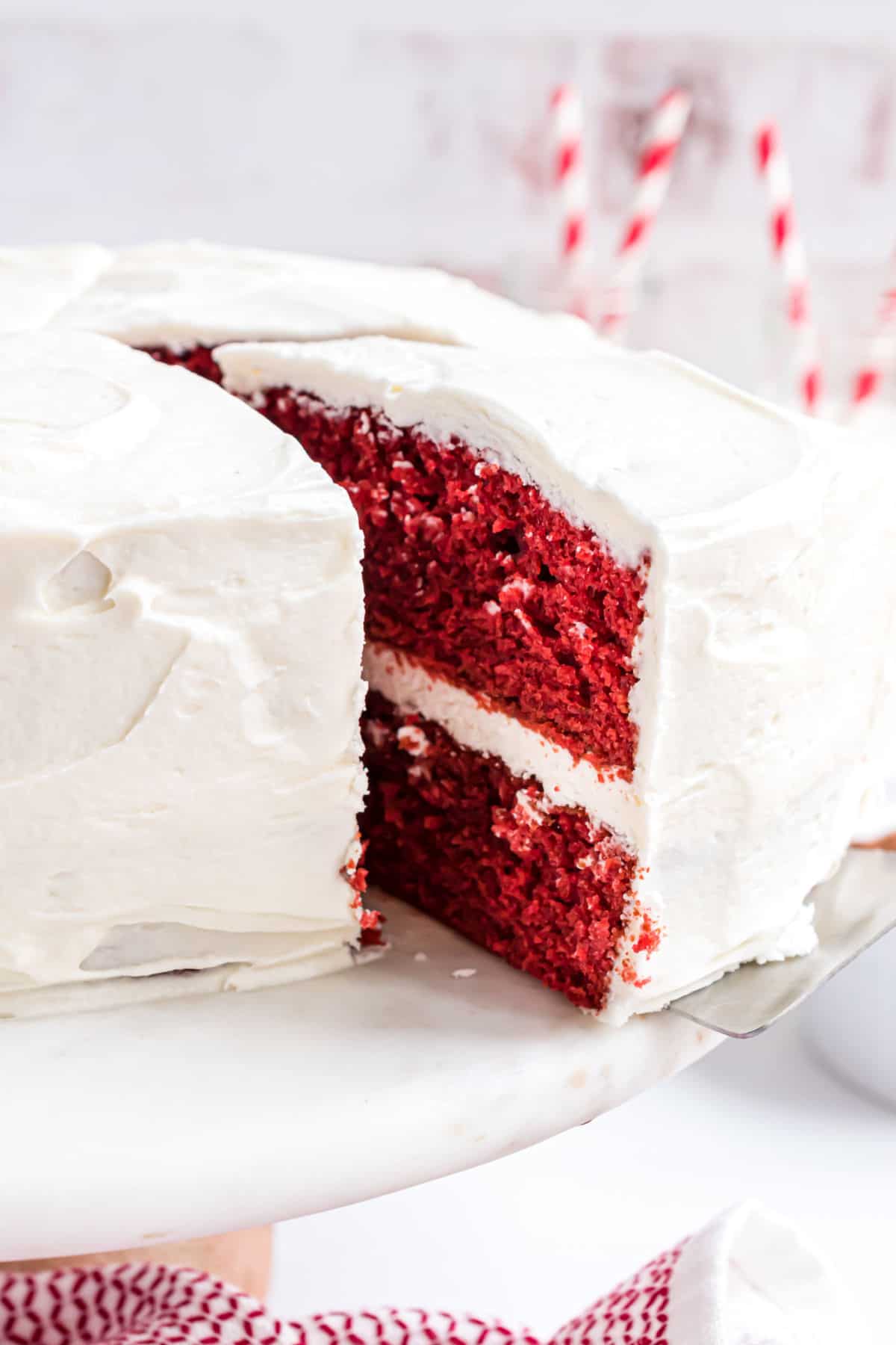 Red velvet layer cake on a white cake platter with a slice being removed.