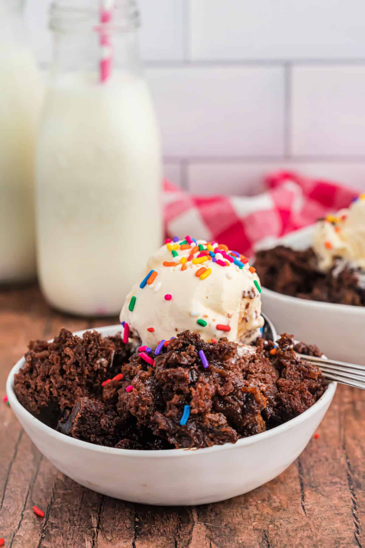 Chocolate hot fudge cake in a white bowl topped with vanilla ice cream and sprinkles.