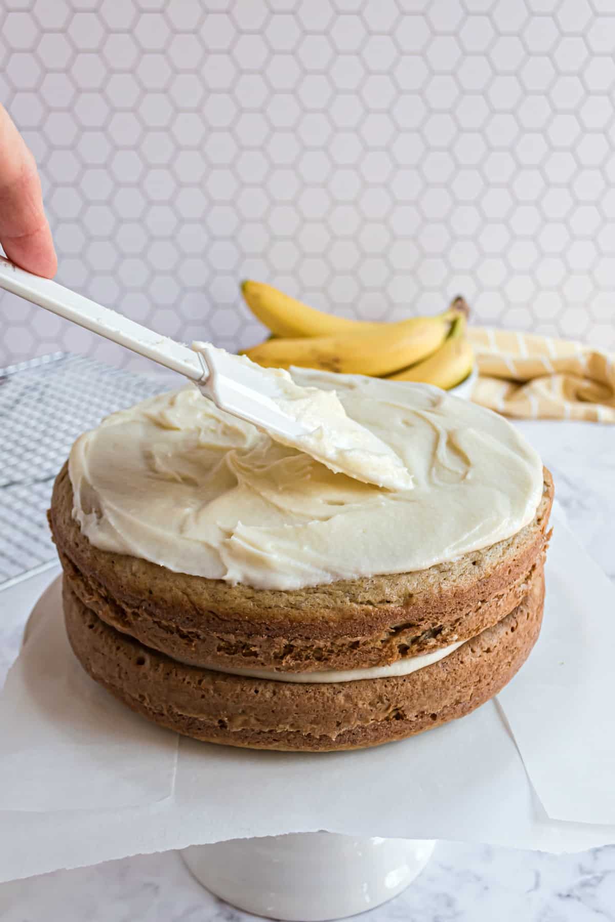 Two cake layers with frosting being spread on top.