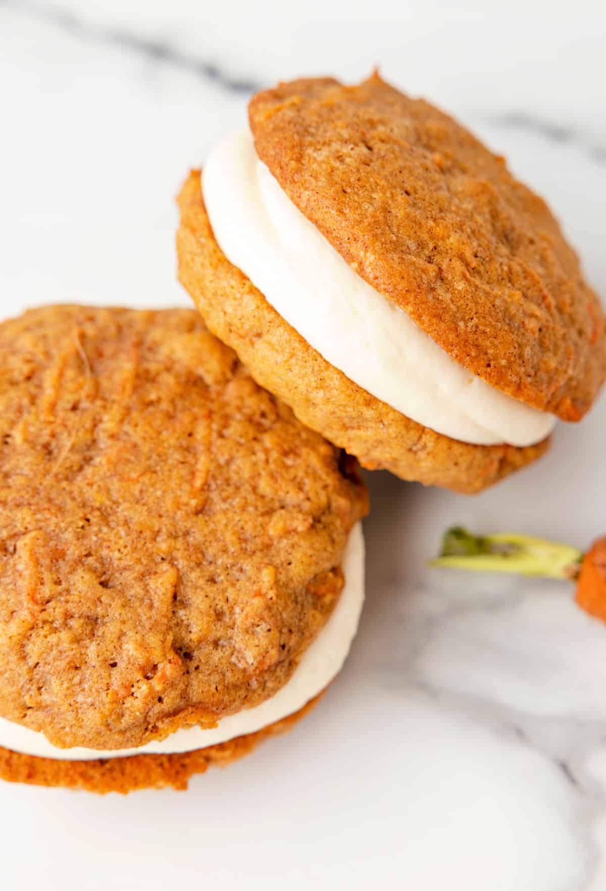 Stack of two carrot cake whoopie pies with cream cheese frosting filling.