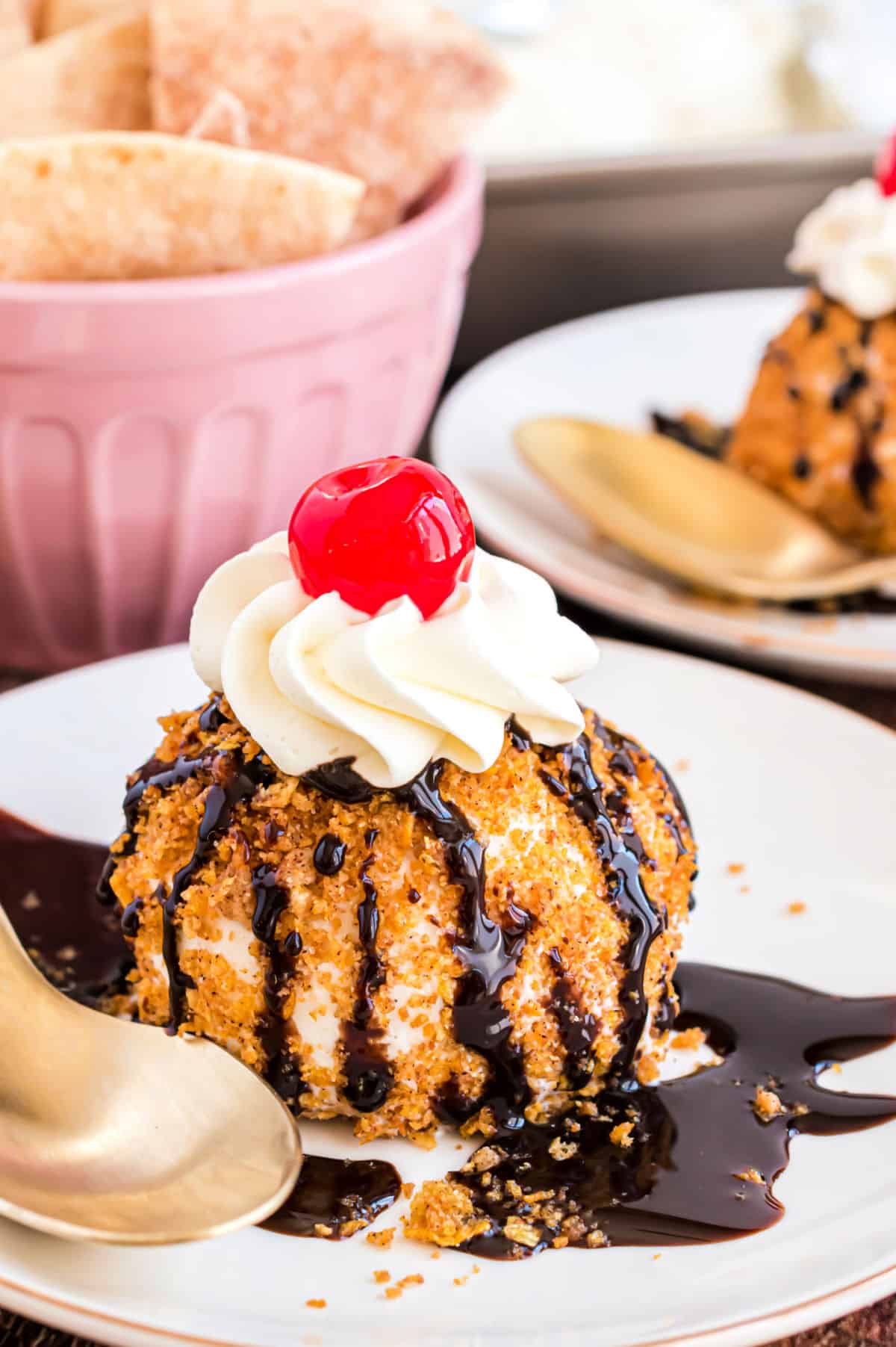 Fried ice cream on a white plate with chocolate syrup, whipped cream, and a cherry.