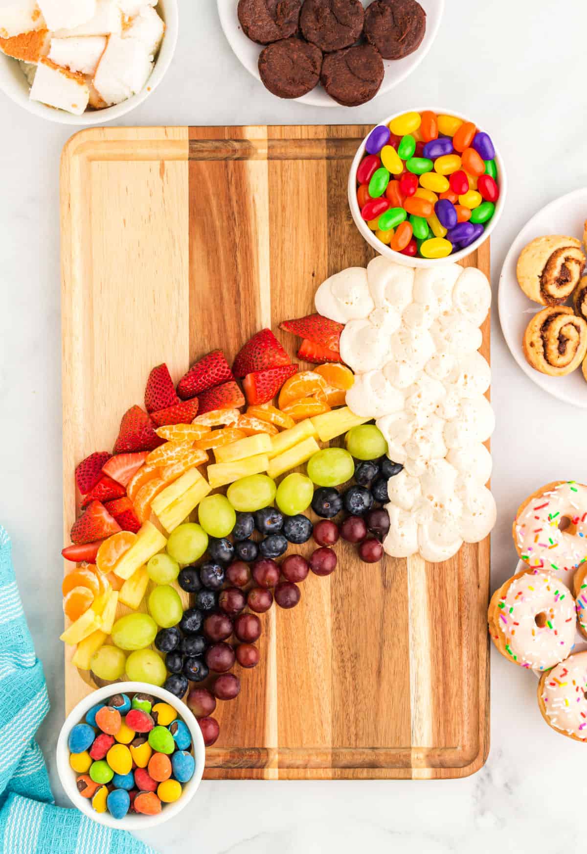 Rainbow of fruit with a cloud of frosting on a wooden board.
