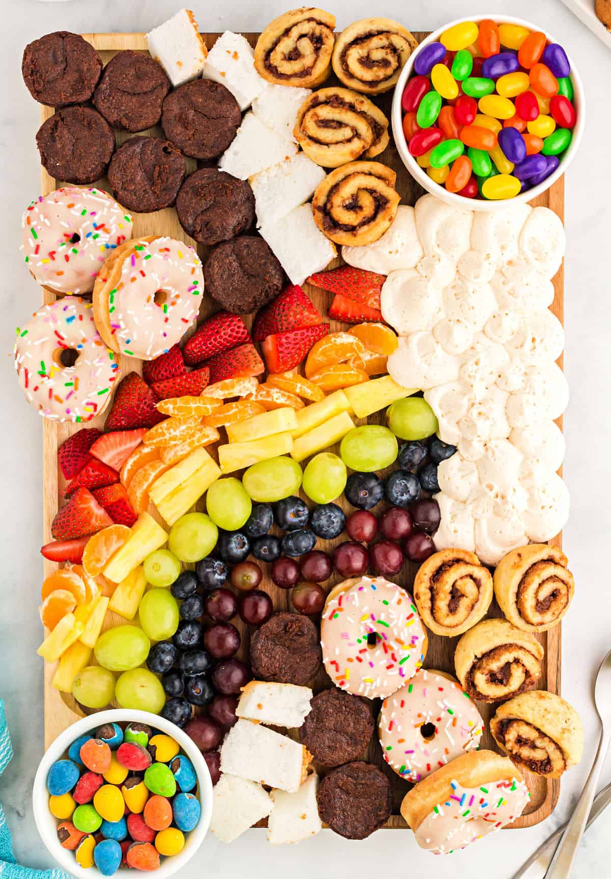 Rainbow buttercream dessert board with fruit, frosting, brownies and donuts.